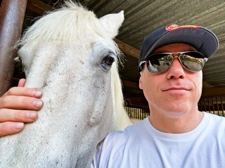 Ian King Los Angeles standing beside a white horse at a stable